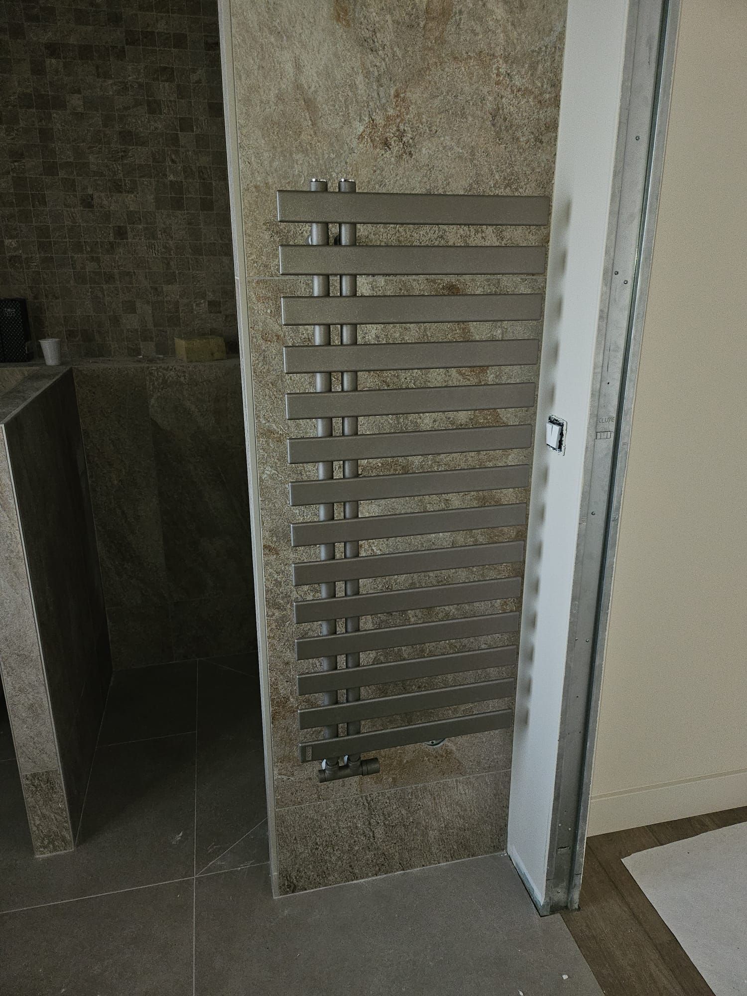 Sèche-serviettes mural en métal dans une salle de bains carrelée, à côté de l'entrée de la douche.