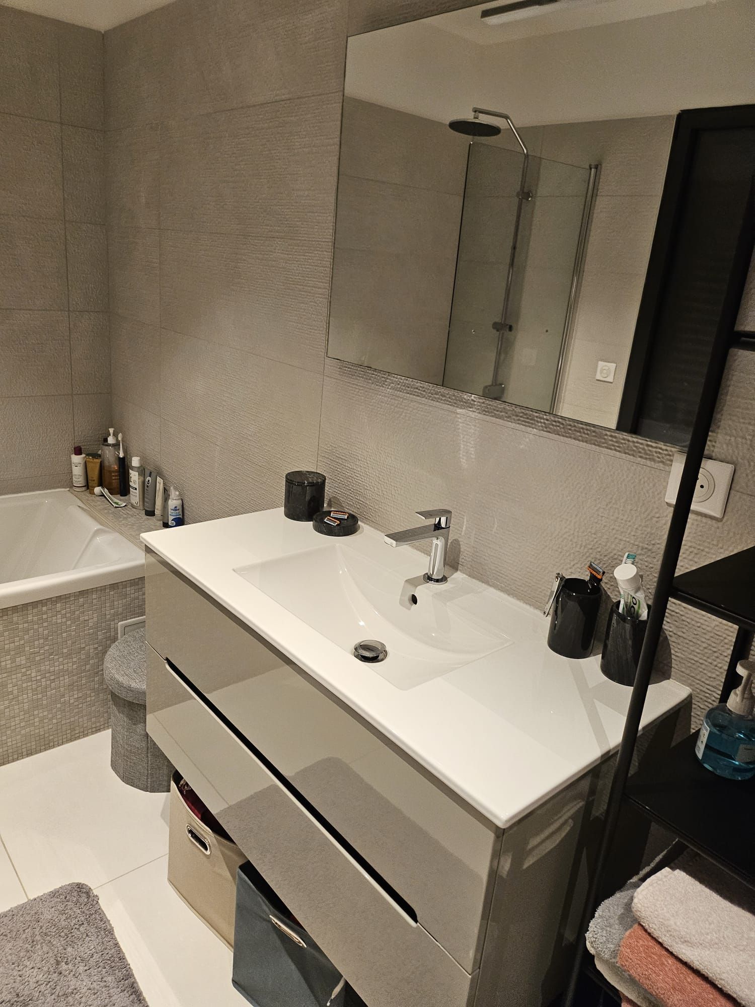 Meuble lavabo moderne avec miroir, lavabo, articles de toilette et serviettes pliées sur un mur carrelé.
