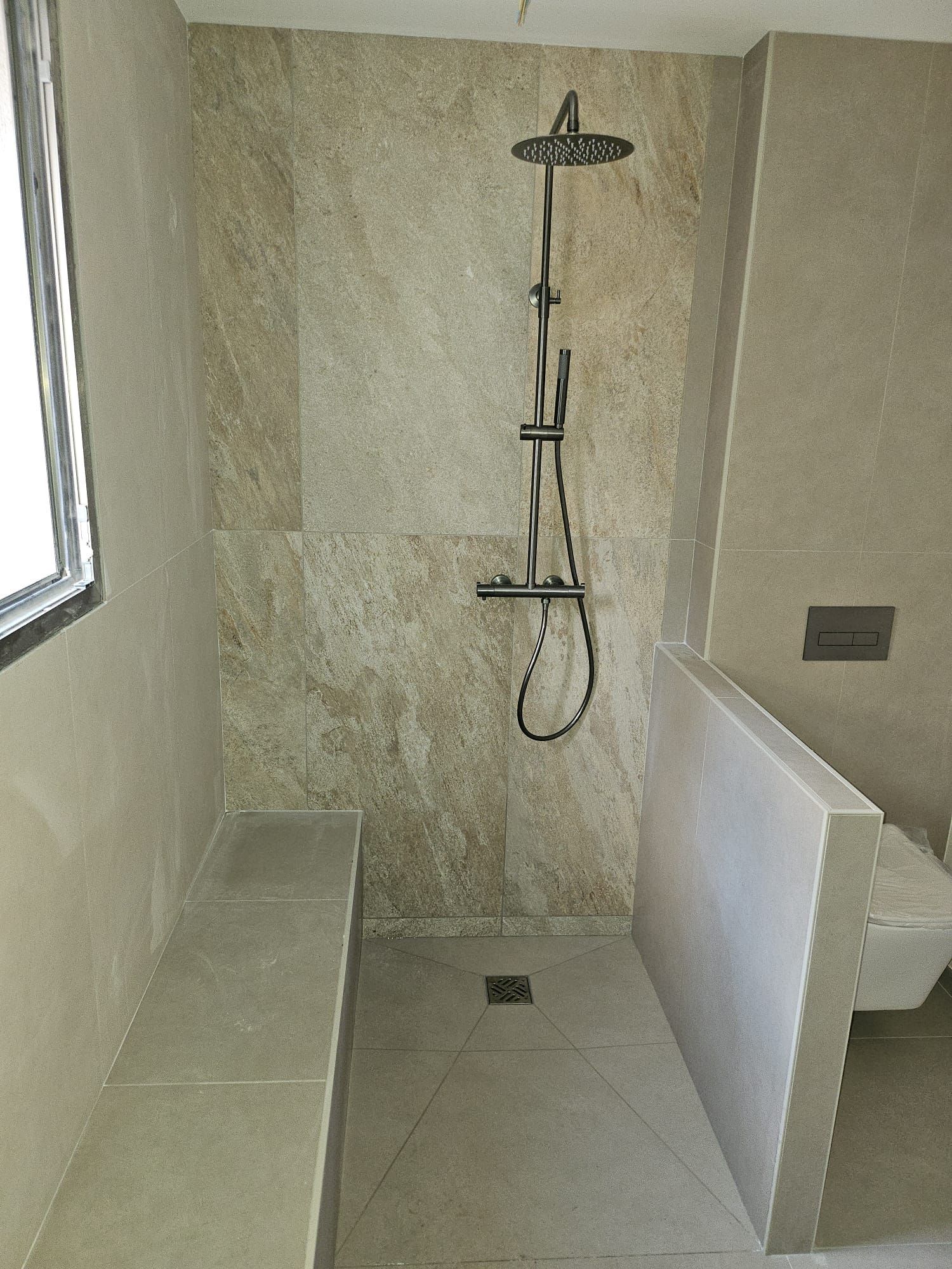 Petite douche accessible avec banc, barres d'appui, pommeau de douche mural et sol carrelé.