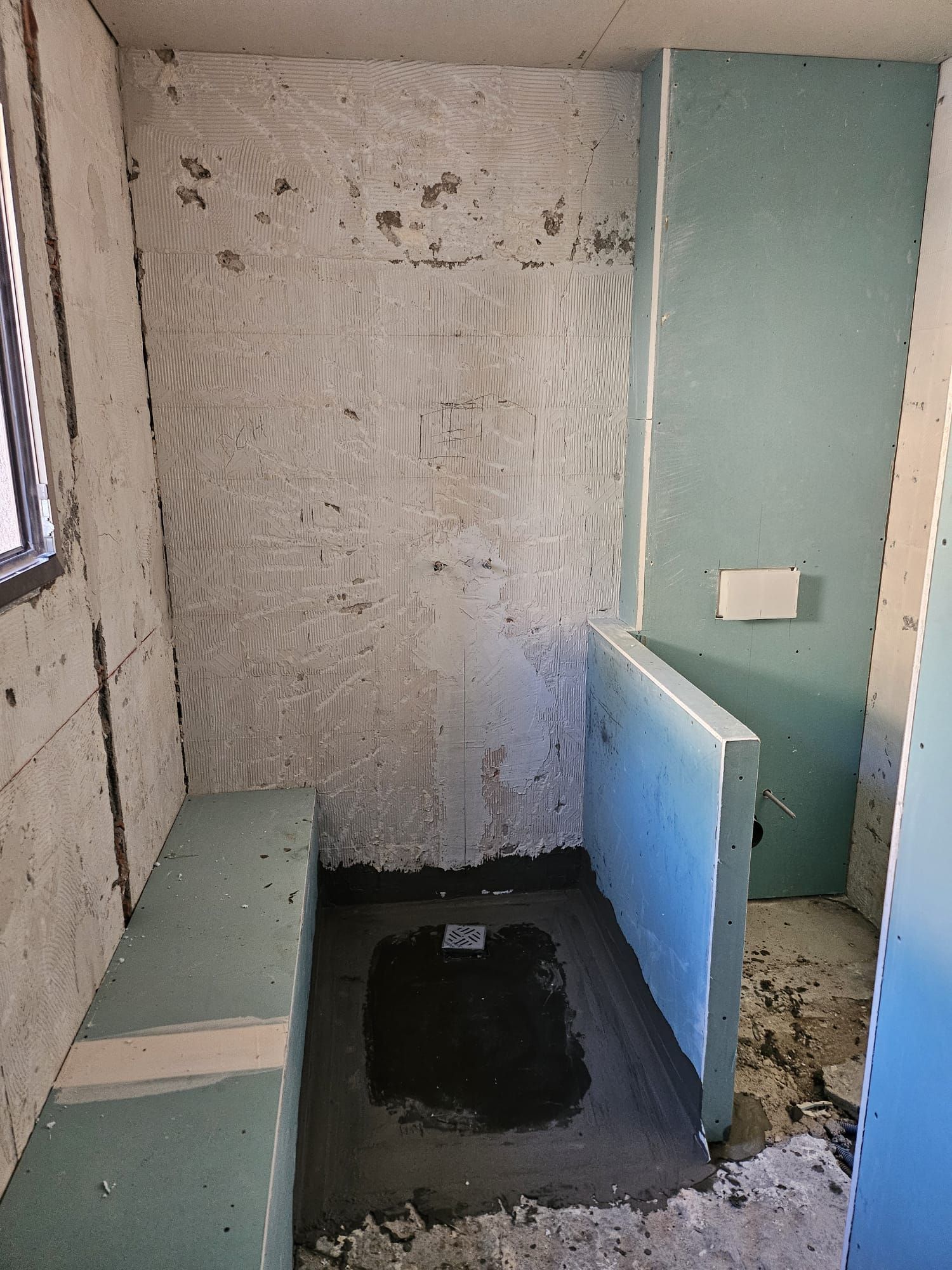 Petite salle de bain aux murs non finis, toilettes supprimées, ouverture apparente dans le sol et panneau de séparation turquoise
