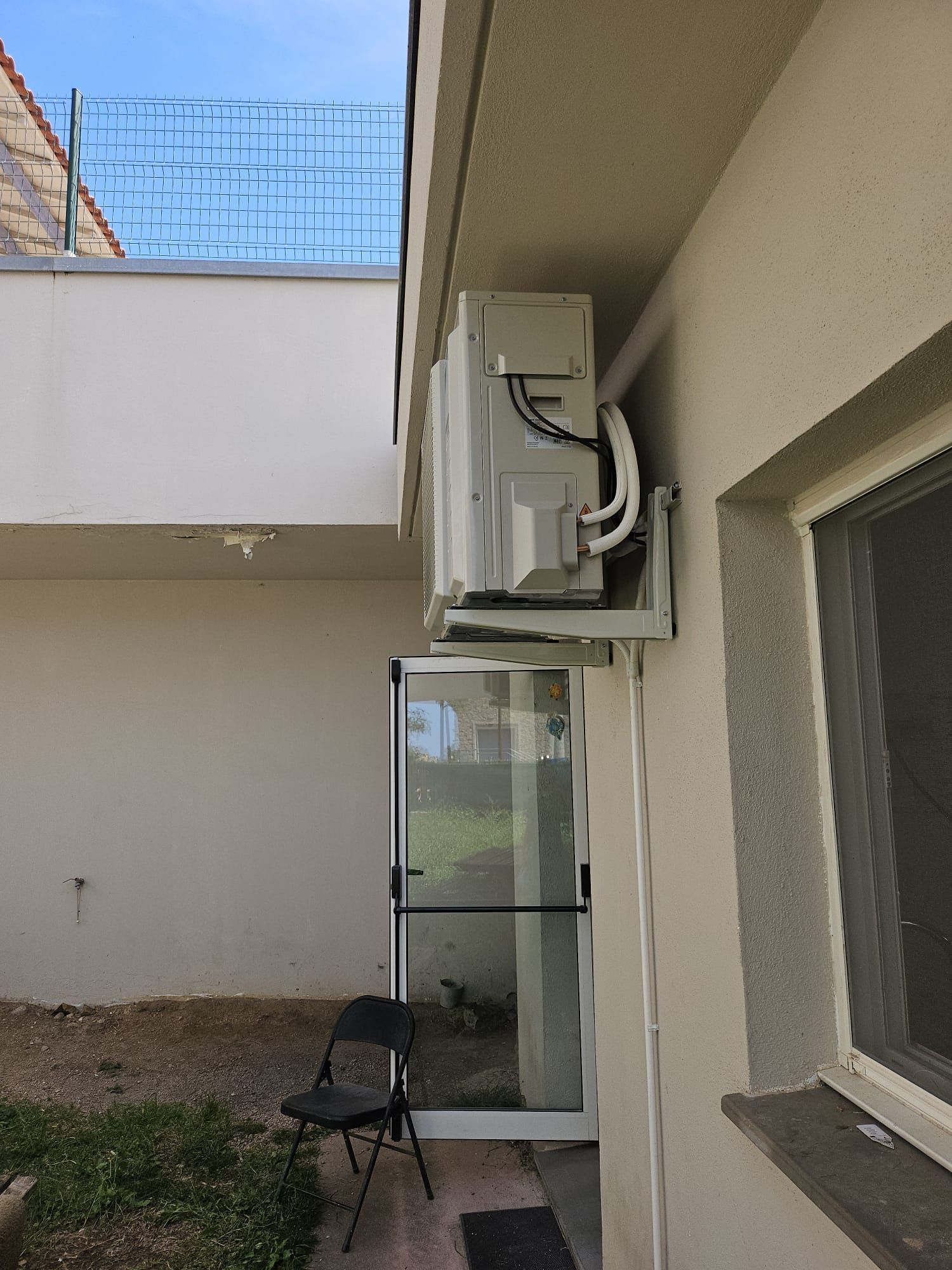 Terrasse extérieure avec un climatiseur mural au-dessus d'une porte vitrée et une chaise en dessous.