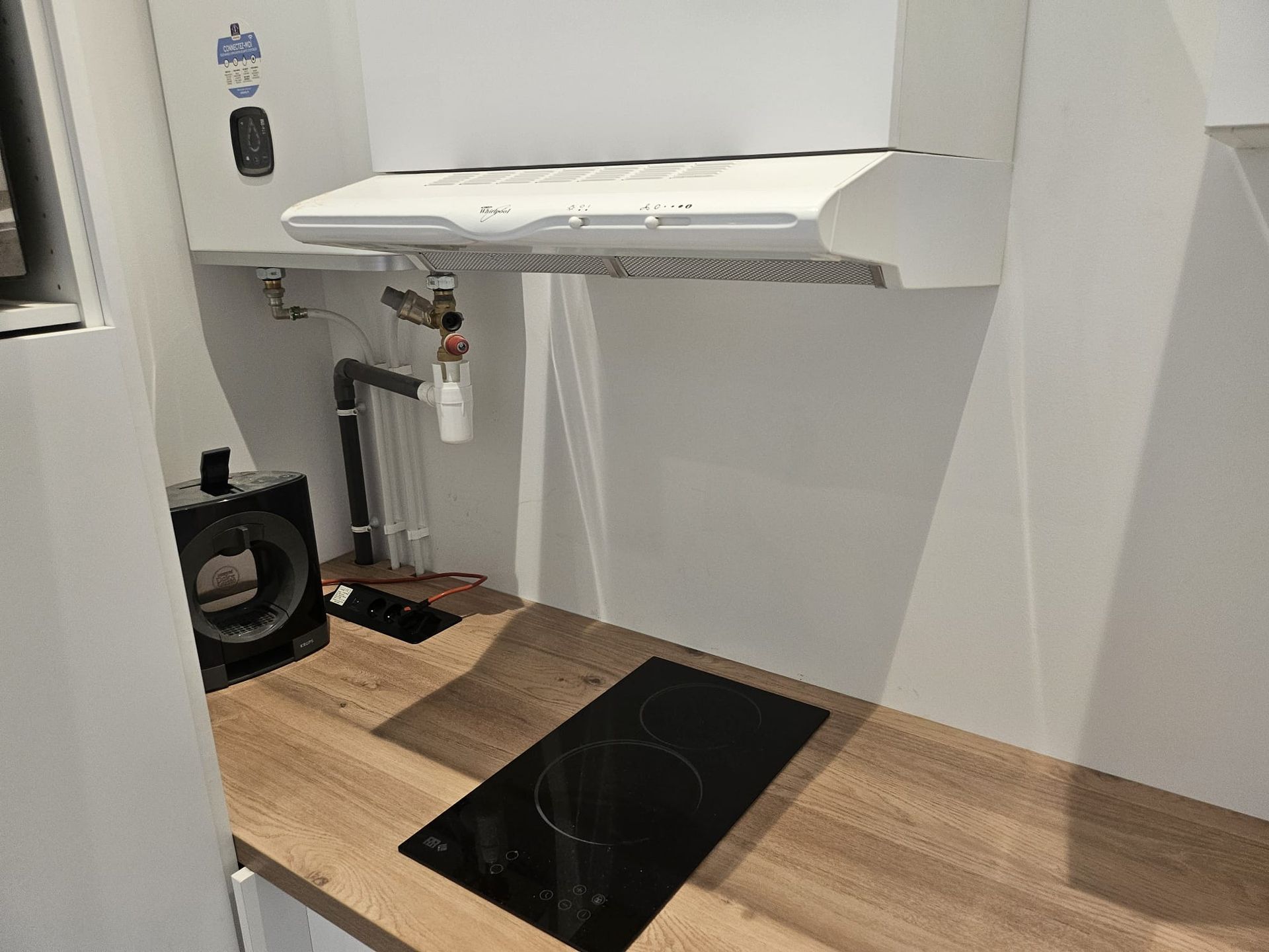 Petite cuisine avec placards blancs, parquet, plaque de cuisson noire et hotte murale.