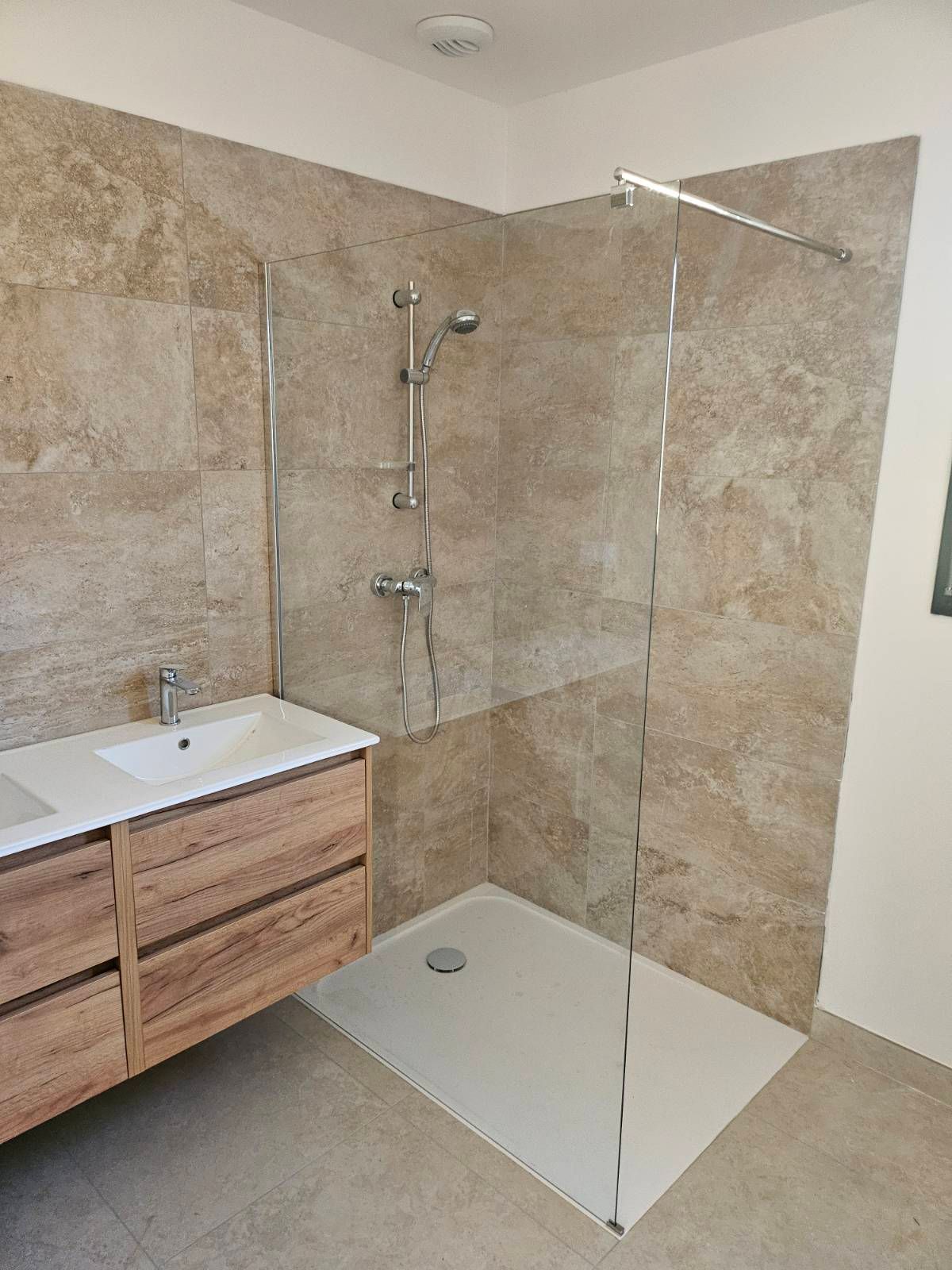 Salle de bains moderne avec meuble-lavabo en bois, lavabo et douche à l'italienne en verre aux murs carrelés beiges