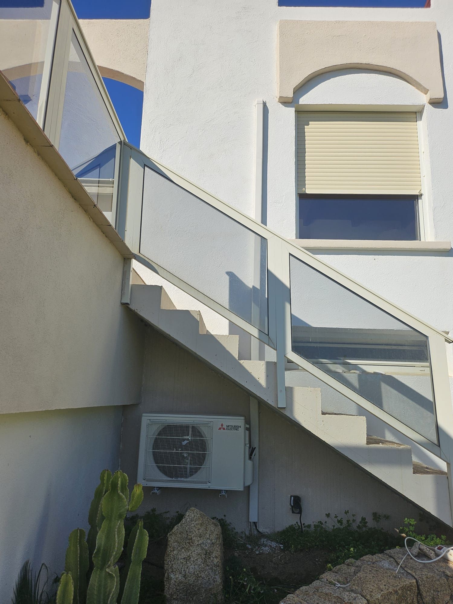 Escalier extérieur jouxtant un bâtiment en stuc blanc avec une fenêtre fermée et de petites plantes en dessous
