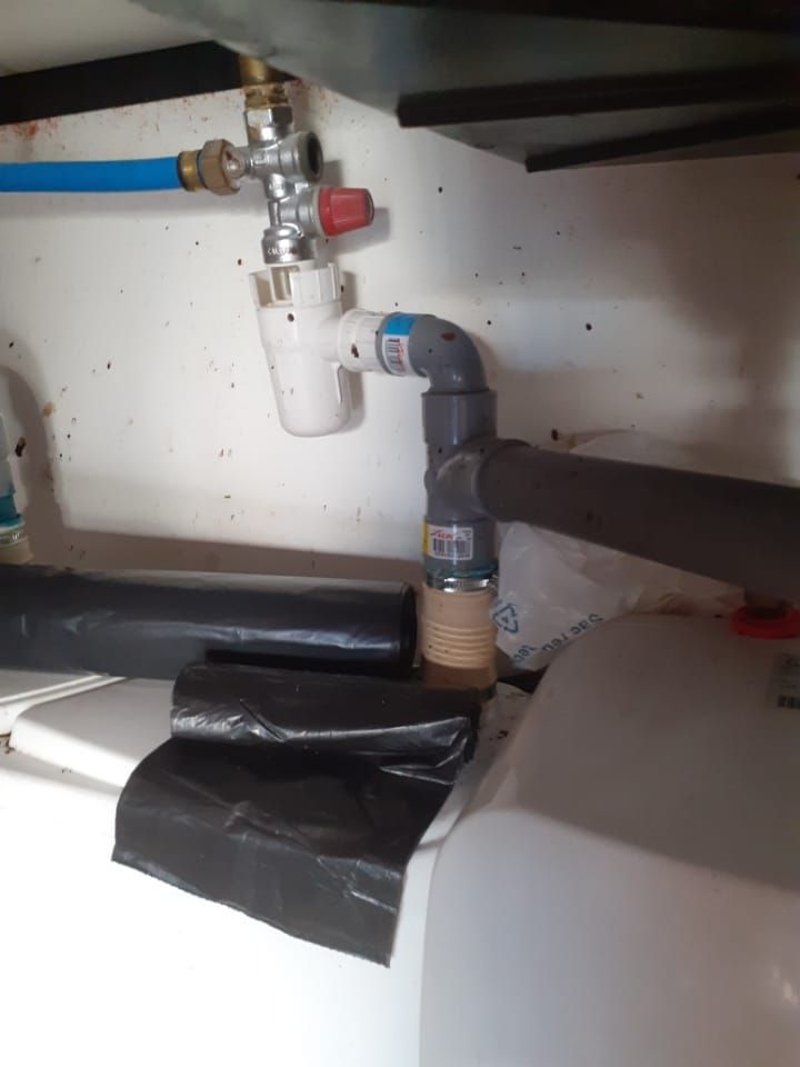 Plomberie sous l'évier avec tuyau blanc, vanne bleue et raccords scotchés sur un réservoir d'eau