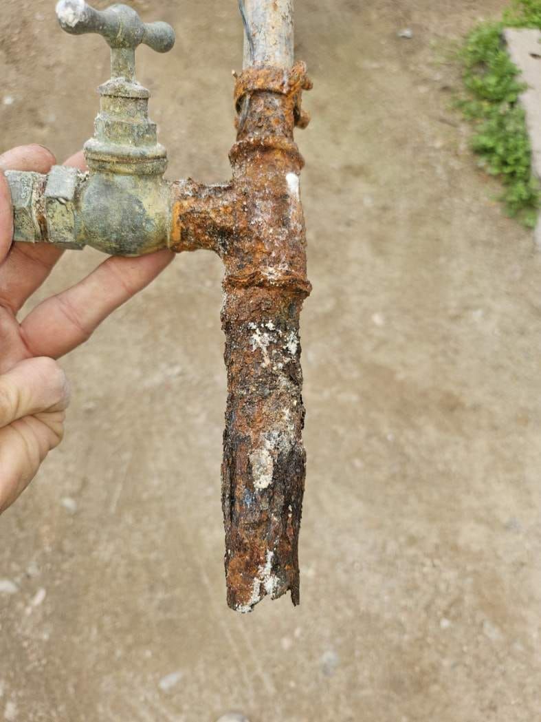 Robinet d'eau extérieur corrodé avec une section de tuyau fortement rouillée tenue par une main