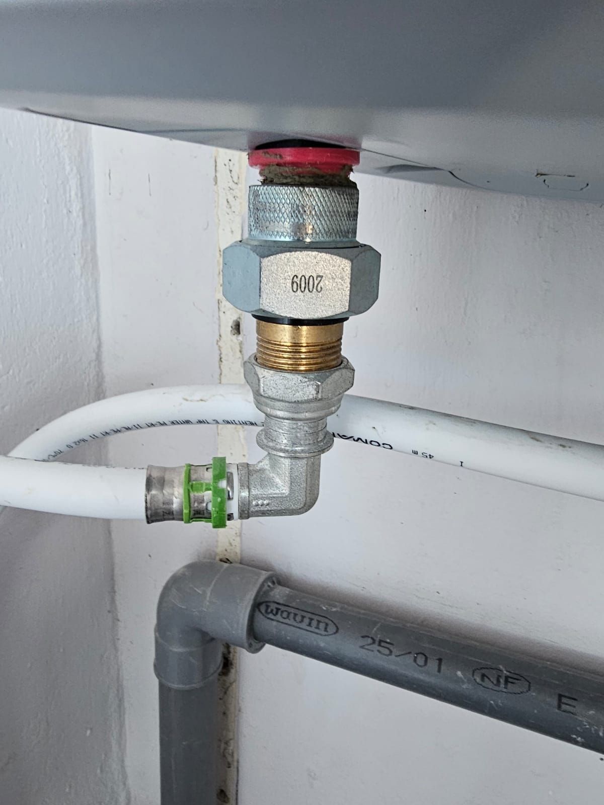 Gros plan sur un robinet et ses raccords de plomberie sous un évier, avec des tuyaux blancs et gris.