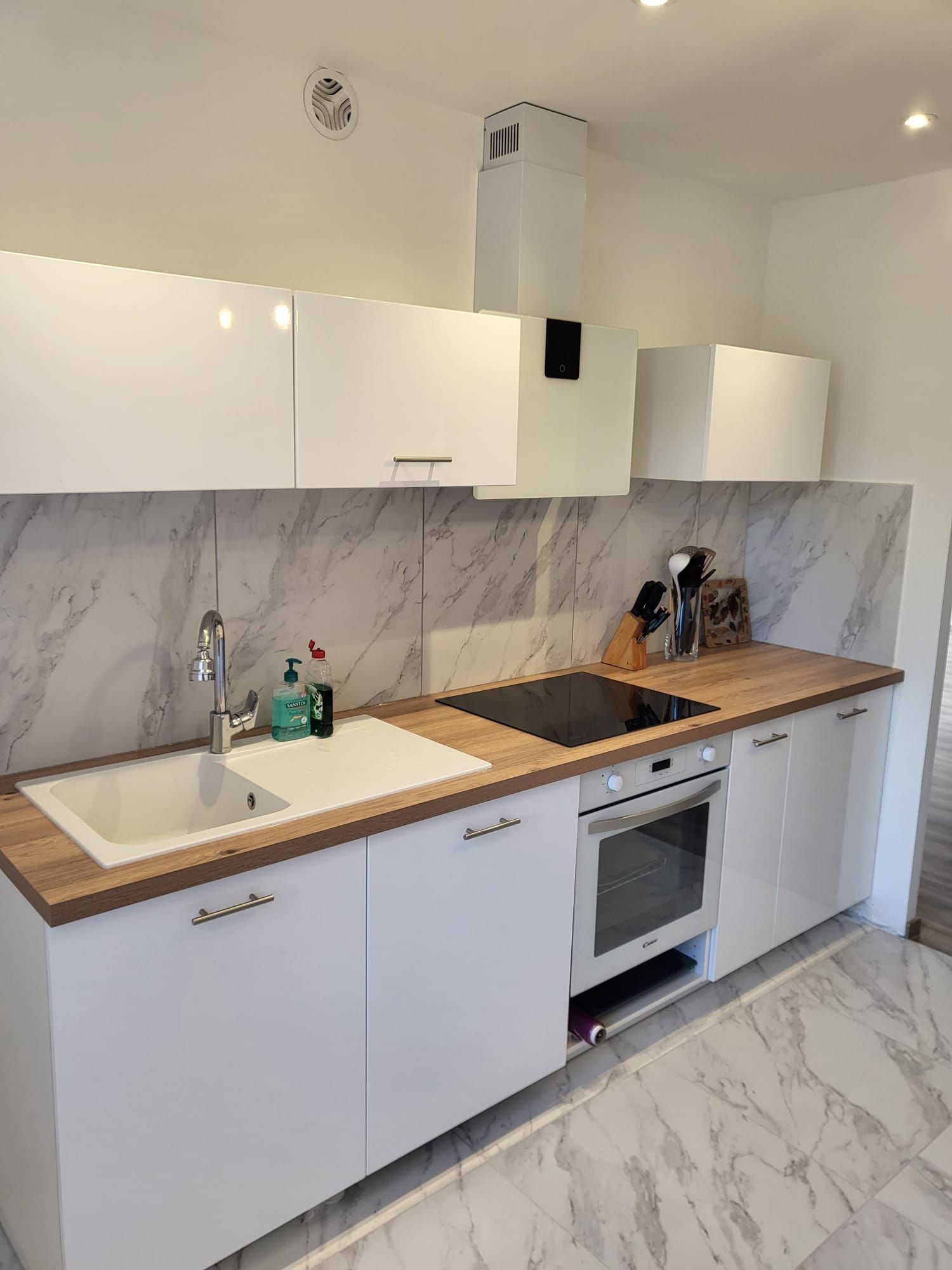 Cuisine blanche moderne avec crédence en marbre, plans de travail en bois, évier, plaque de cuisson et four.