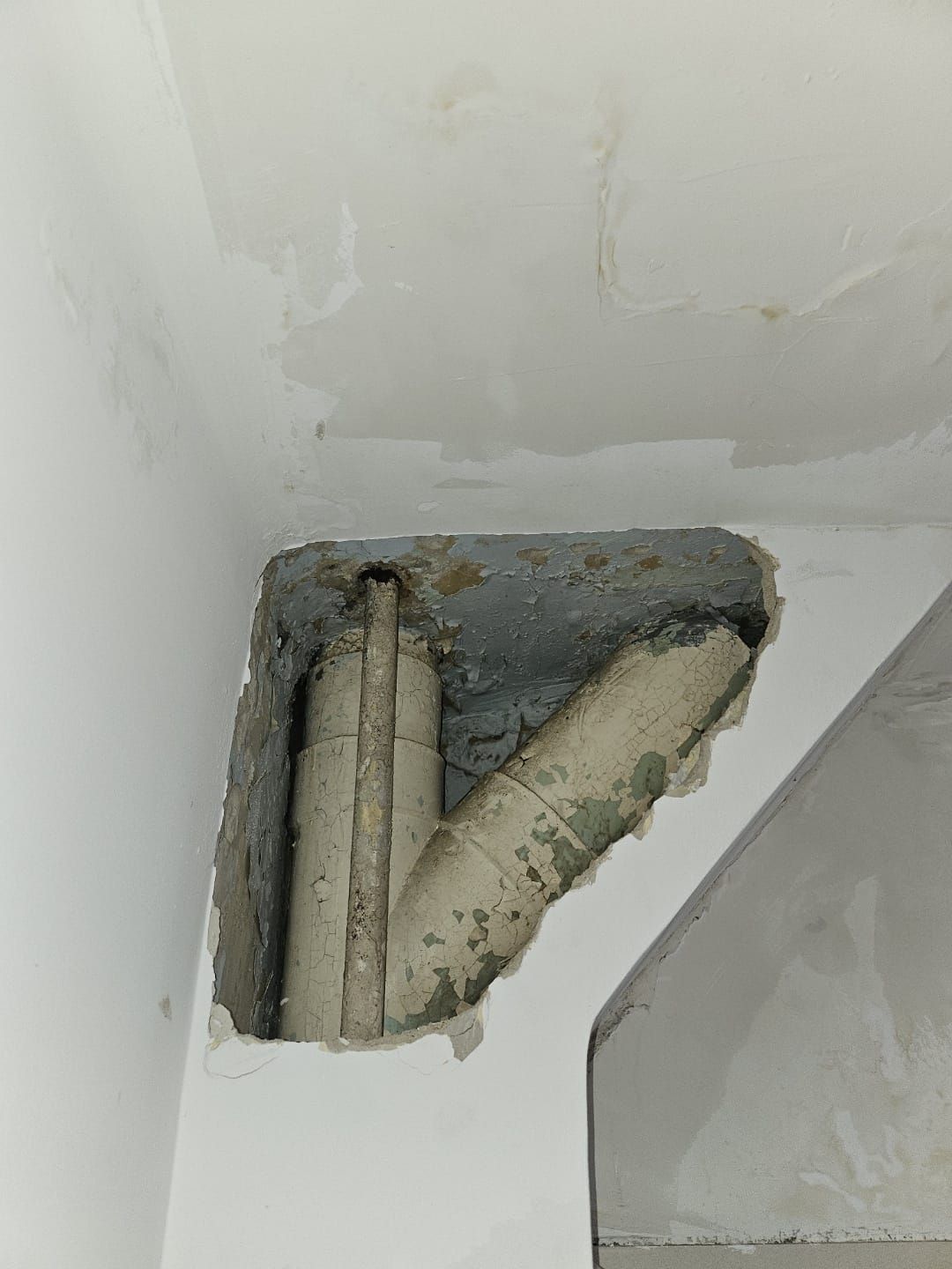 Tuyaux apparents et ouverture dans un mur brut dans un coin intérieur blanc, révélant des travaux de construction inachevés