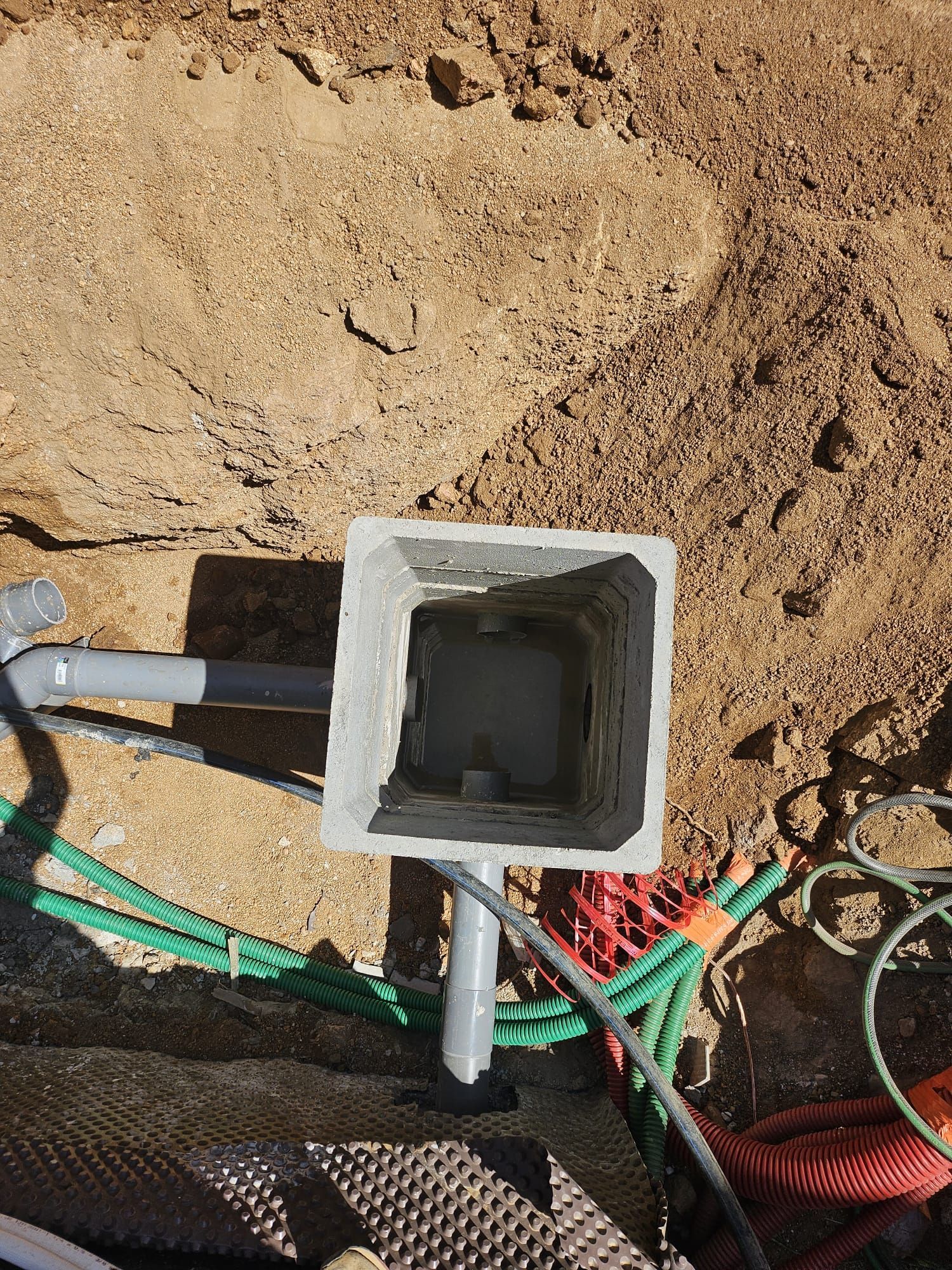 Conduit utilitaire carré ouvert dans la terre avec tuyaux apparents et câbles colorés autour.