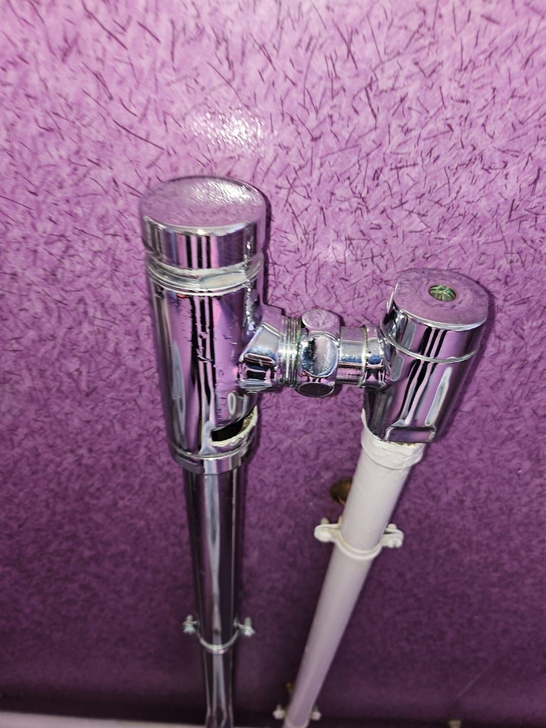 Robinetterie de salle de bain chromée avec un tuyau blanc sur un mur texturé violet