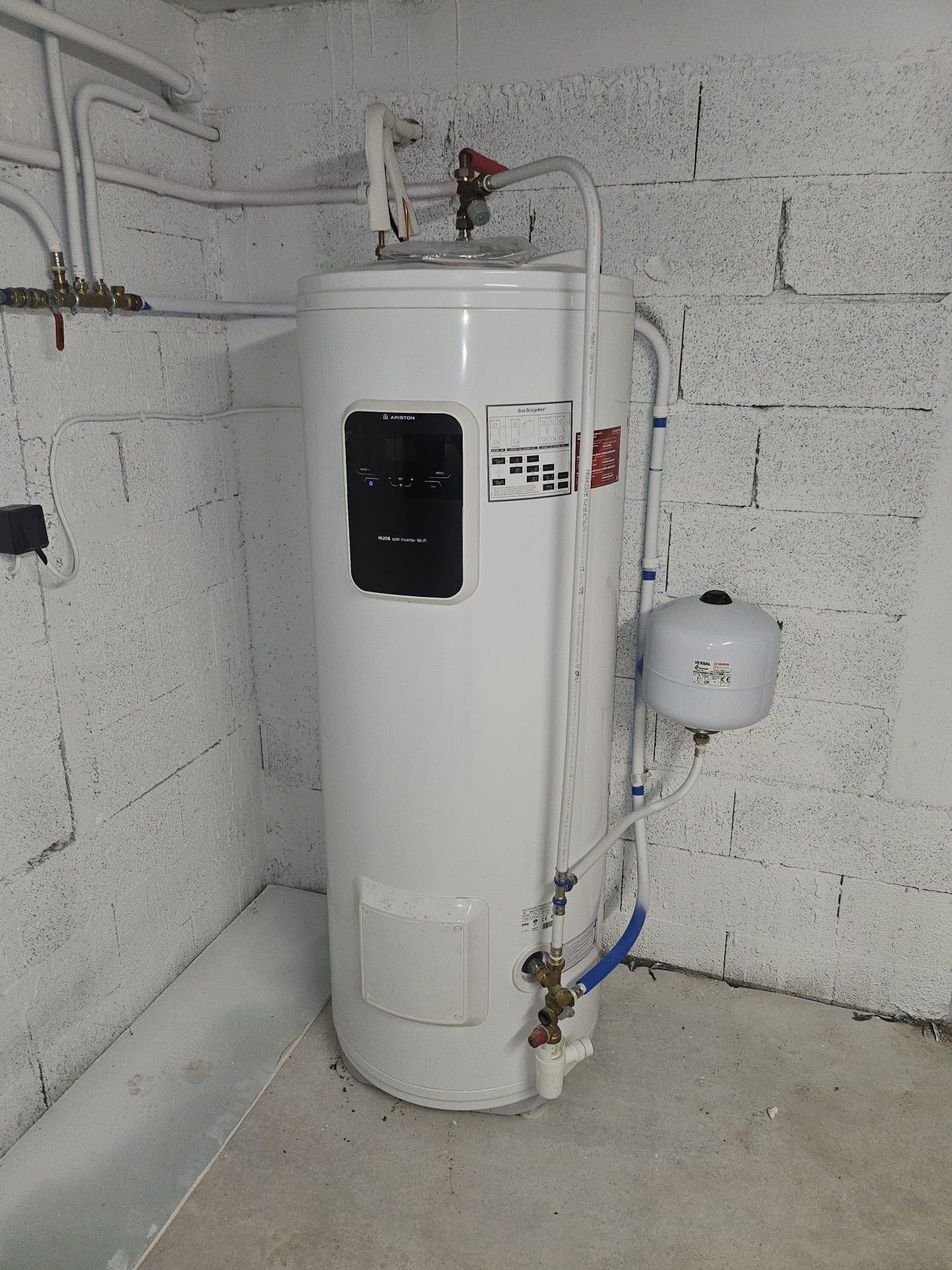 Chauffe-eau blanc avec tuyaux et vannes dans une buanderie en béton