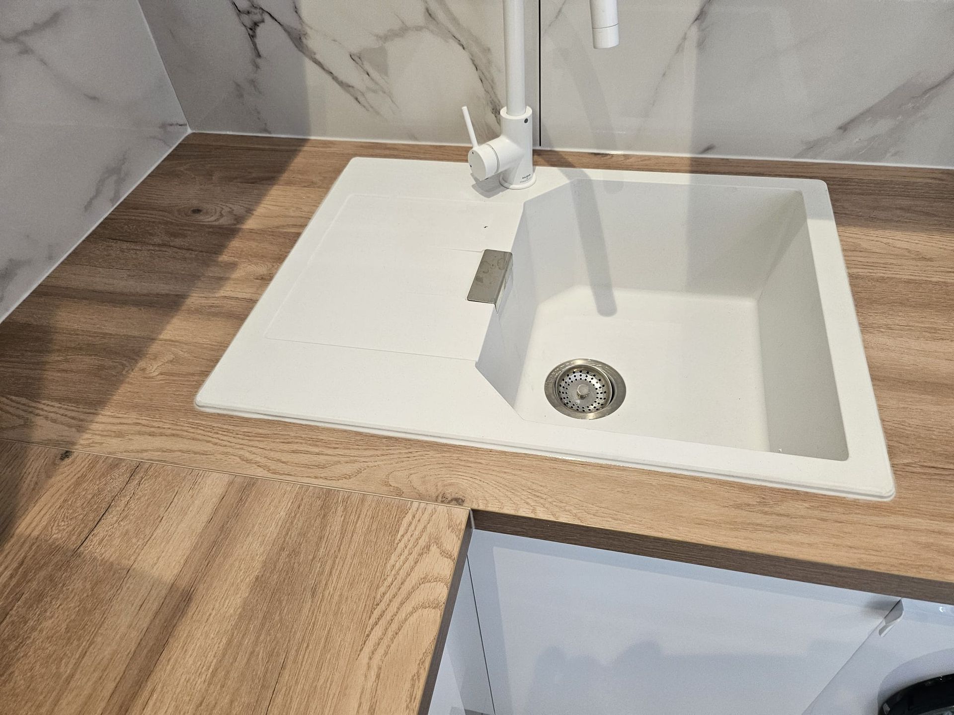 Lavabo de salle de bain blanc avec robinet chromé, intégré dans un comptoir imitation bois et une crédence en carrelage de marbre.