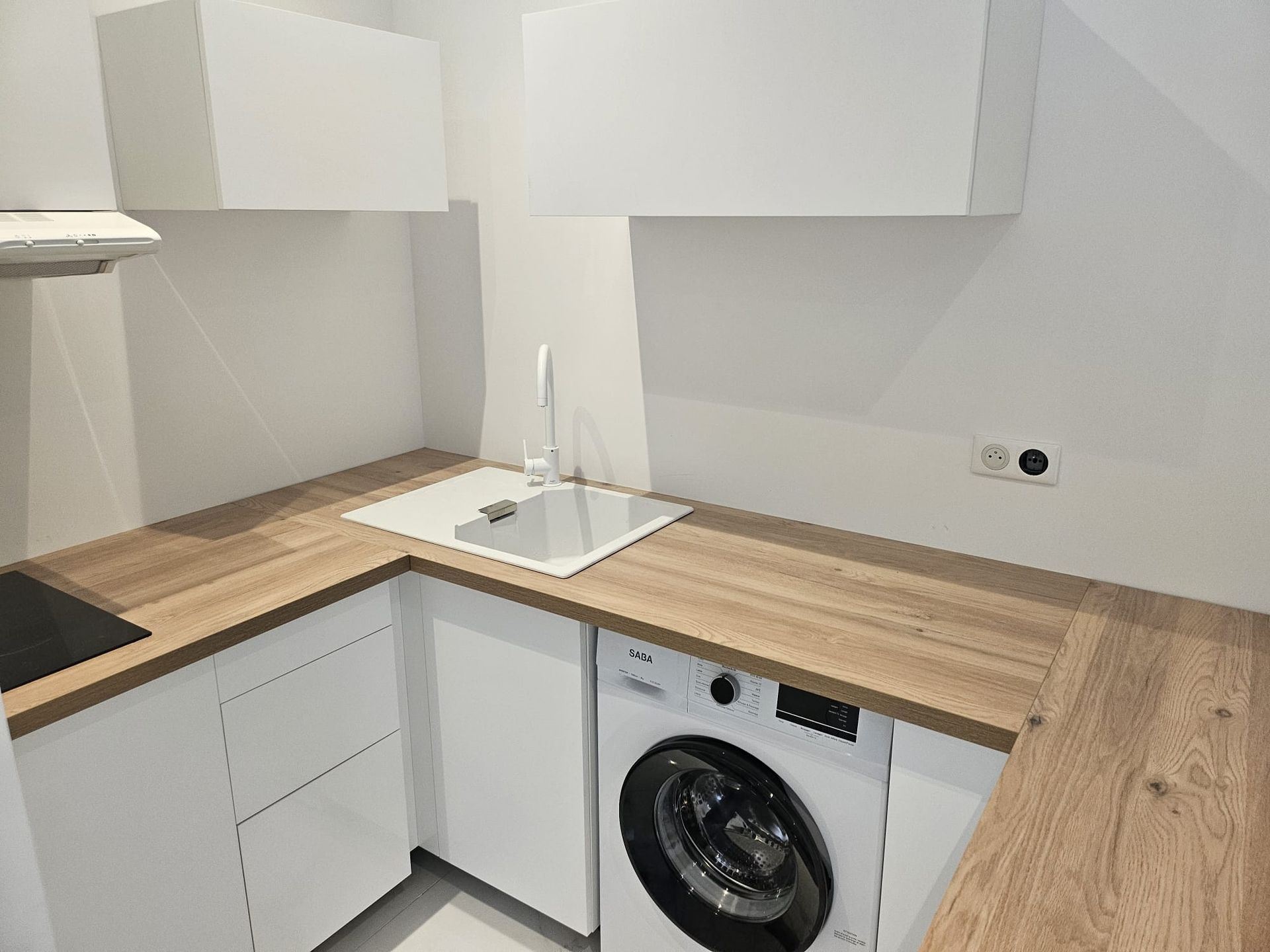 Cuisine moderne blanche avec comptoirs en bois, évier et lave-linge sous le plan de travail.