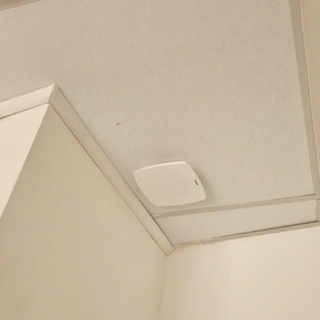 Coin de plafond avec un détecteur de fumée blanc installé près d'un panneau lumineux encastré.