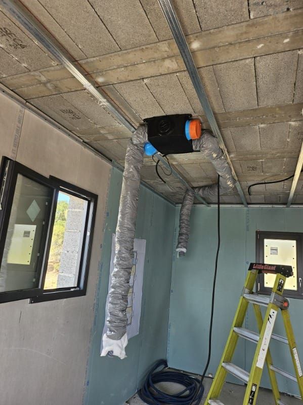 Pièce partiellement aménagée avec conduits de ventilation apparents au plafond, une fenêtre, une échelle et des outils de construction