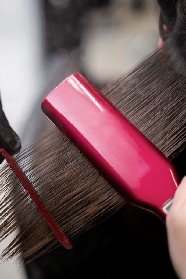 Plancha alisadora rosa sujetando un mechón de pelo castaño