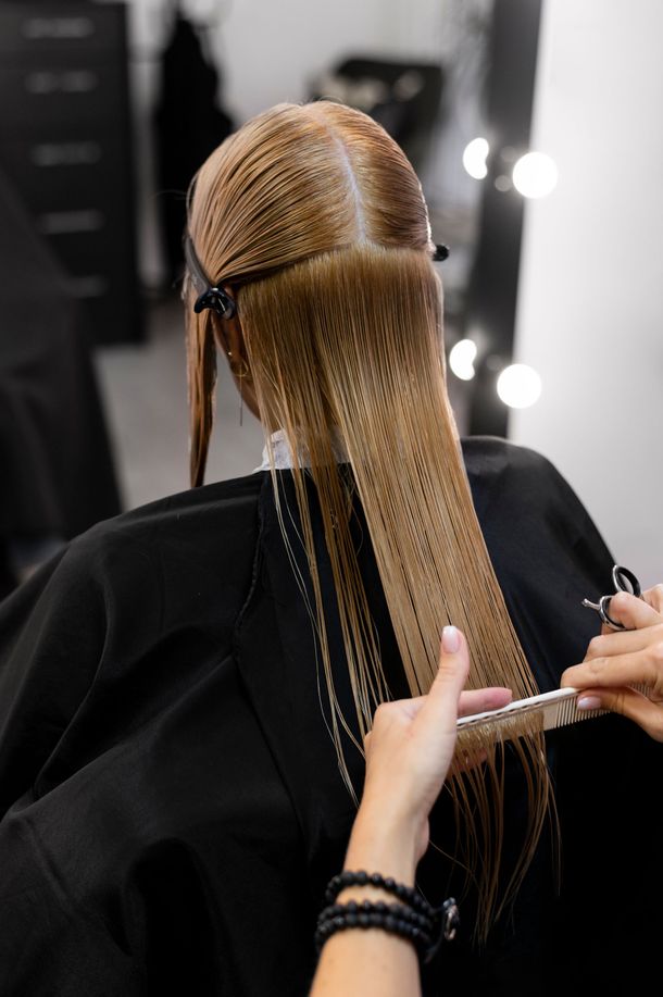 Estilista trenzando el pelo largo y rubio en un salón, con luces de espejo al fondo