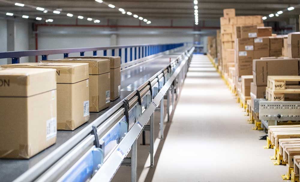 Kisten auf Förderband im Lager, rechts Kistenstapel.