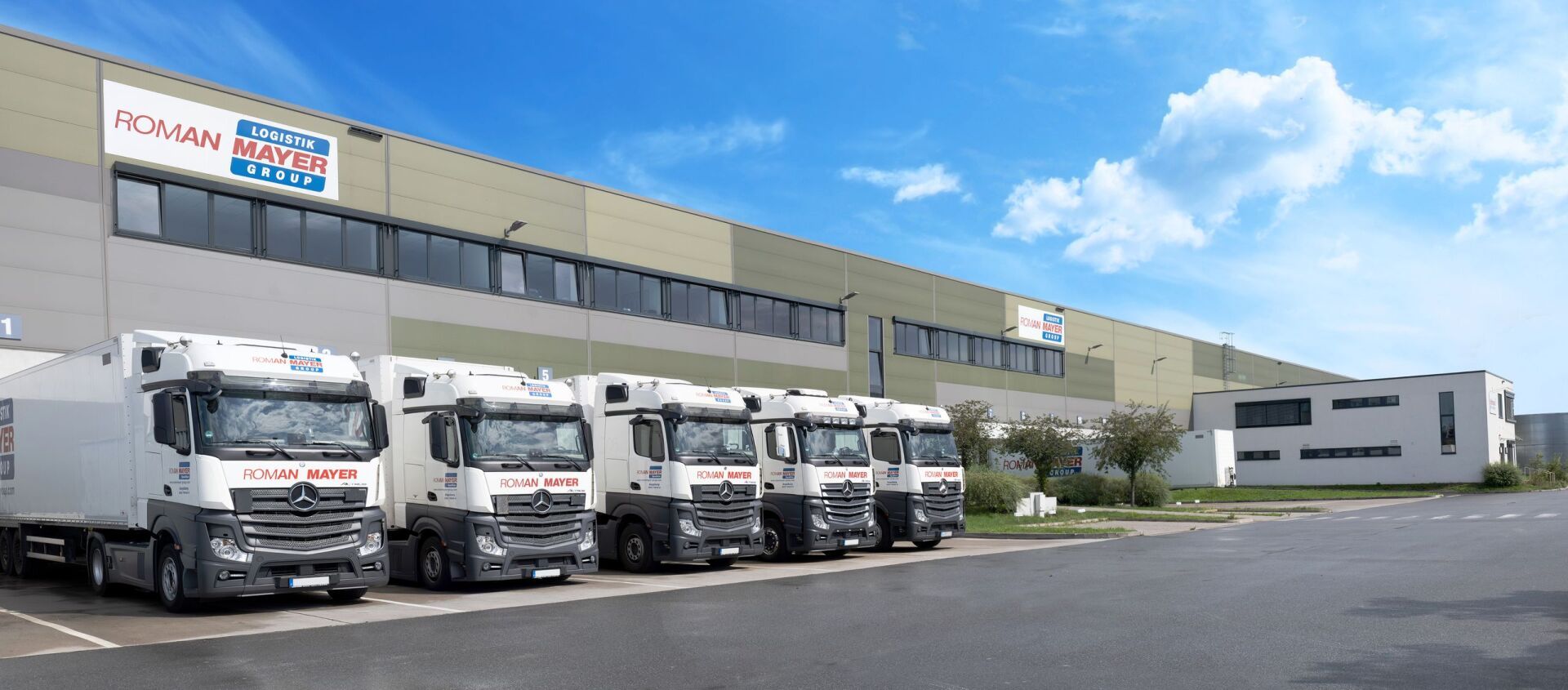 Vor einem großen Lagerhaus mit blauem Himmel und Wolken parken Lastwagen.
