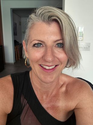 Nahaufnahme-Selfie einer lächelnden Person mit kurzen blonden Haaren, die ein schwarzes One-Shoulder-Top.