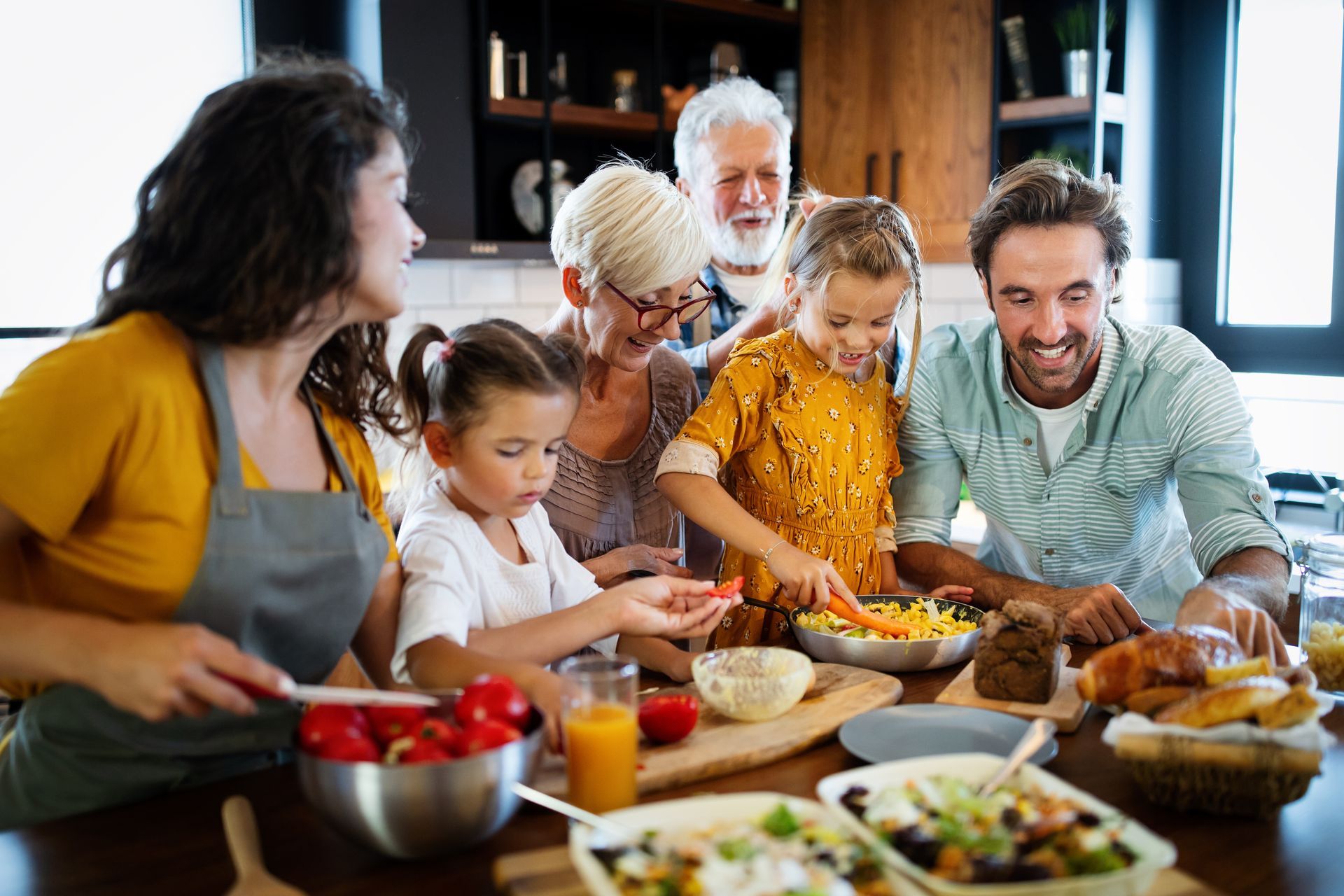 Une famille prépare un repas ensemble autour d'une table de cuisine, partageant la nourriture et souriant.