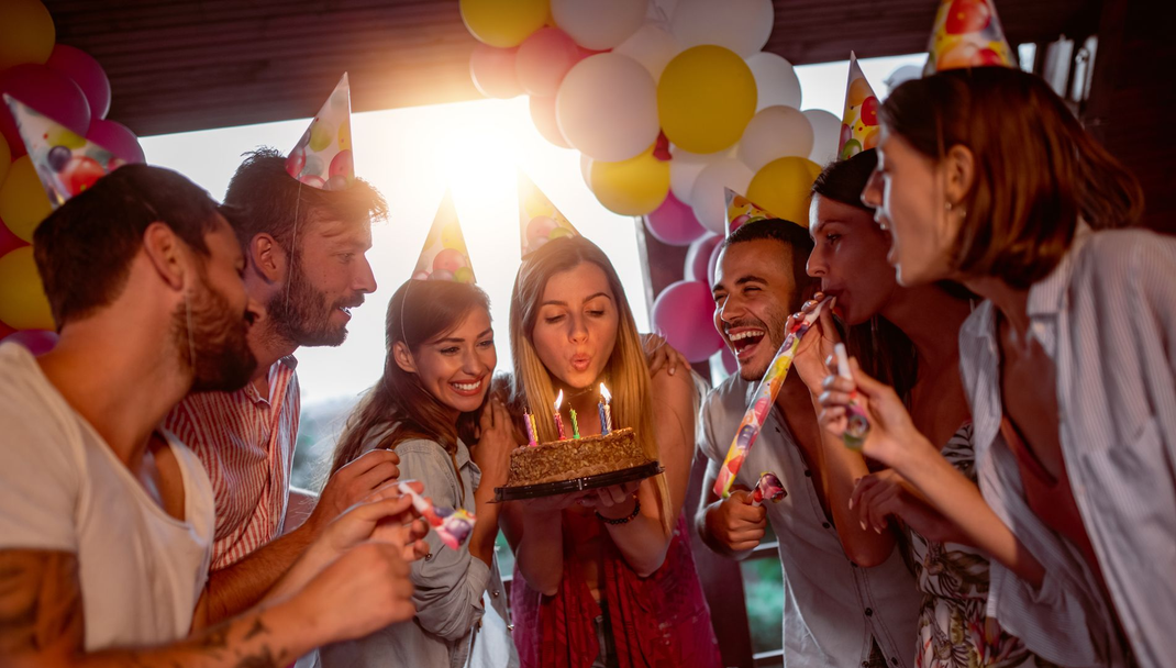 Des amis se rassemblent autour d'un gâteau lors d'une fête d'anniversaire, avec des bougies allumées et des ballons en arrière-plan.