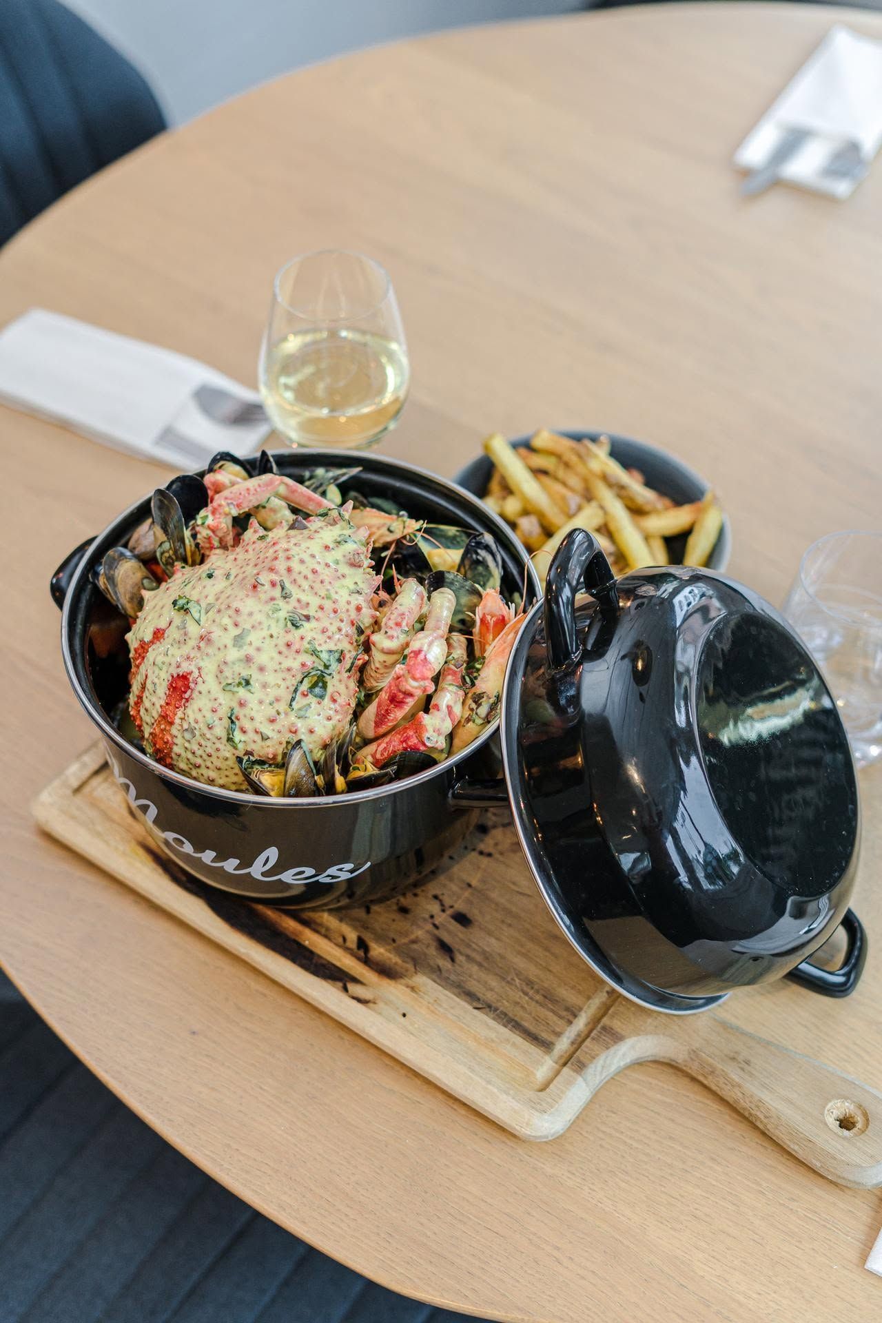 Un pot de pâtes crémeuses avec des frites et du vin sur un plateau en bois, autour d'une table ronde.