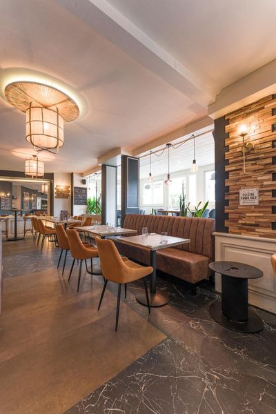 Intérieur de café moderne avec tables en bois, chaises et éclairage chaleureux grâce à de grandes fenêtres.