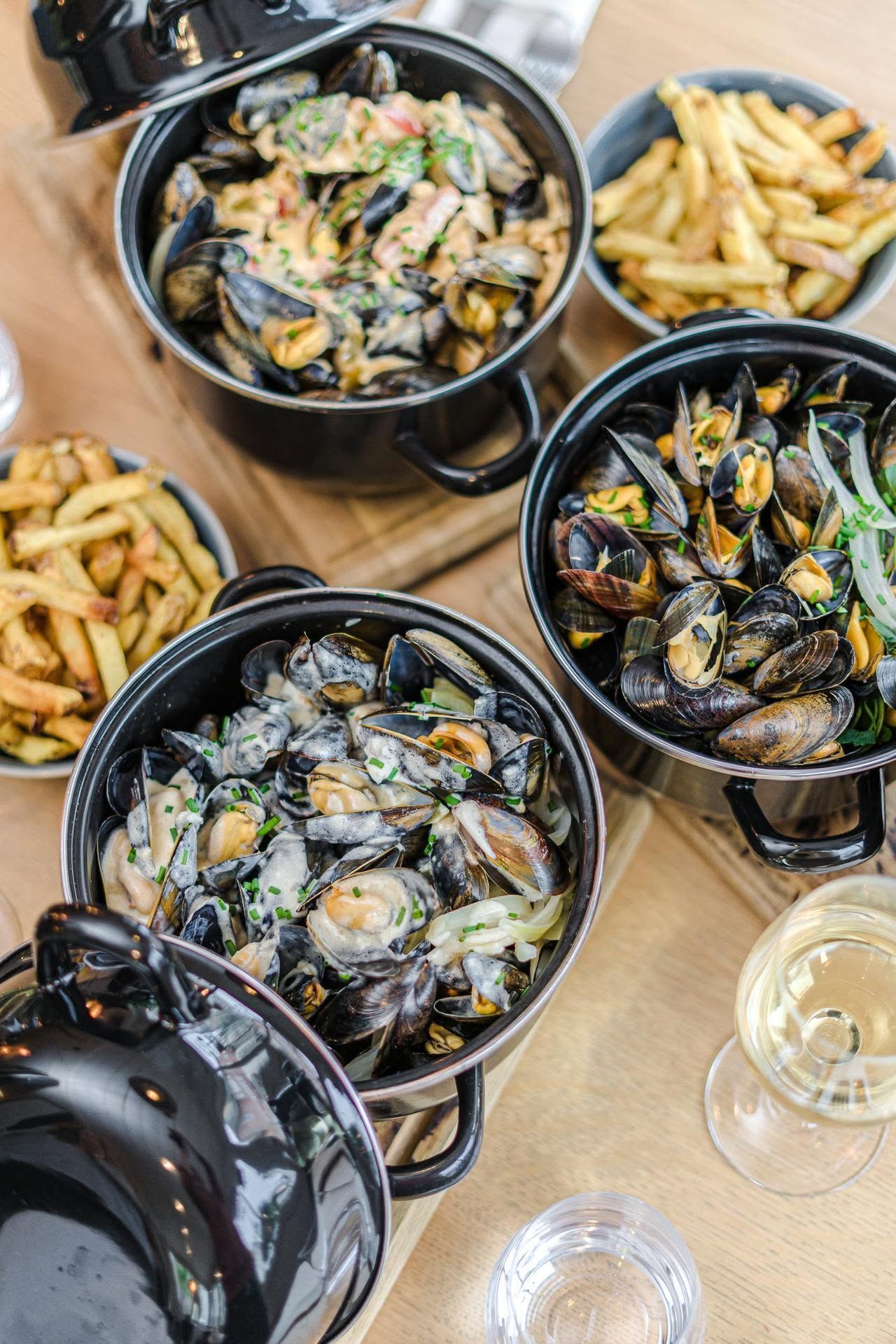 Vue aérienne de moules en cocotte et de frites sur une table, accompagnées d'un verre de vin.