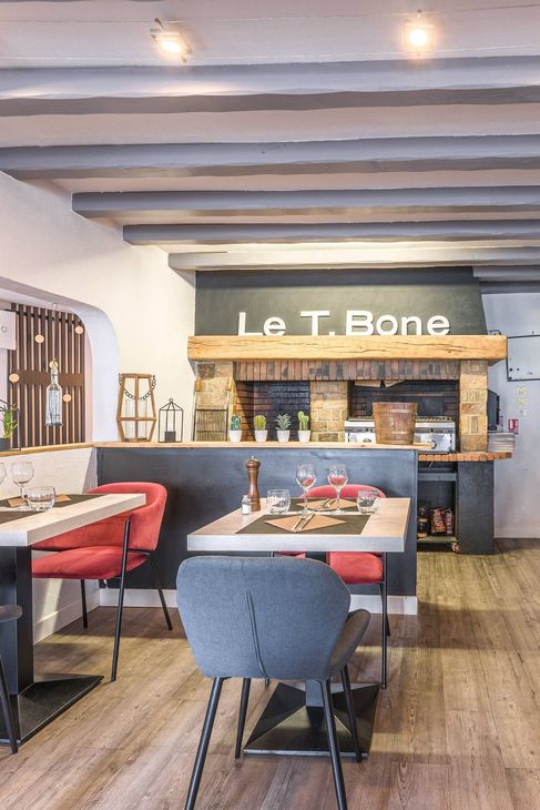 Salle à manger chaleureuse avec banquettes, chaises, poutres apparentes et une enseigne Le T Bone au-dessus du comptoir.