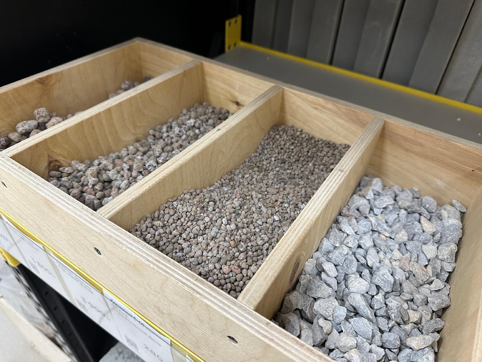 Holztablett, unterteilt in Fächer mit drei verschiedenen Größen von grauem Kies und Steinen.