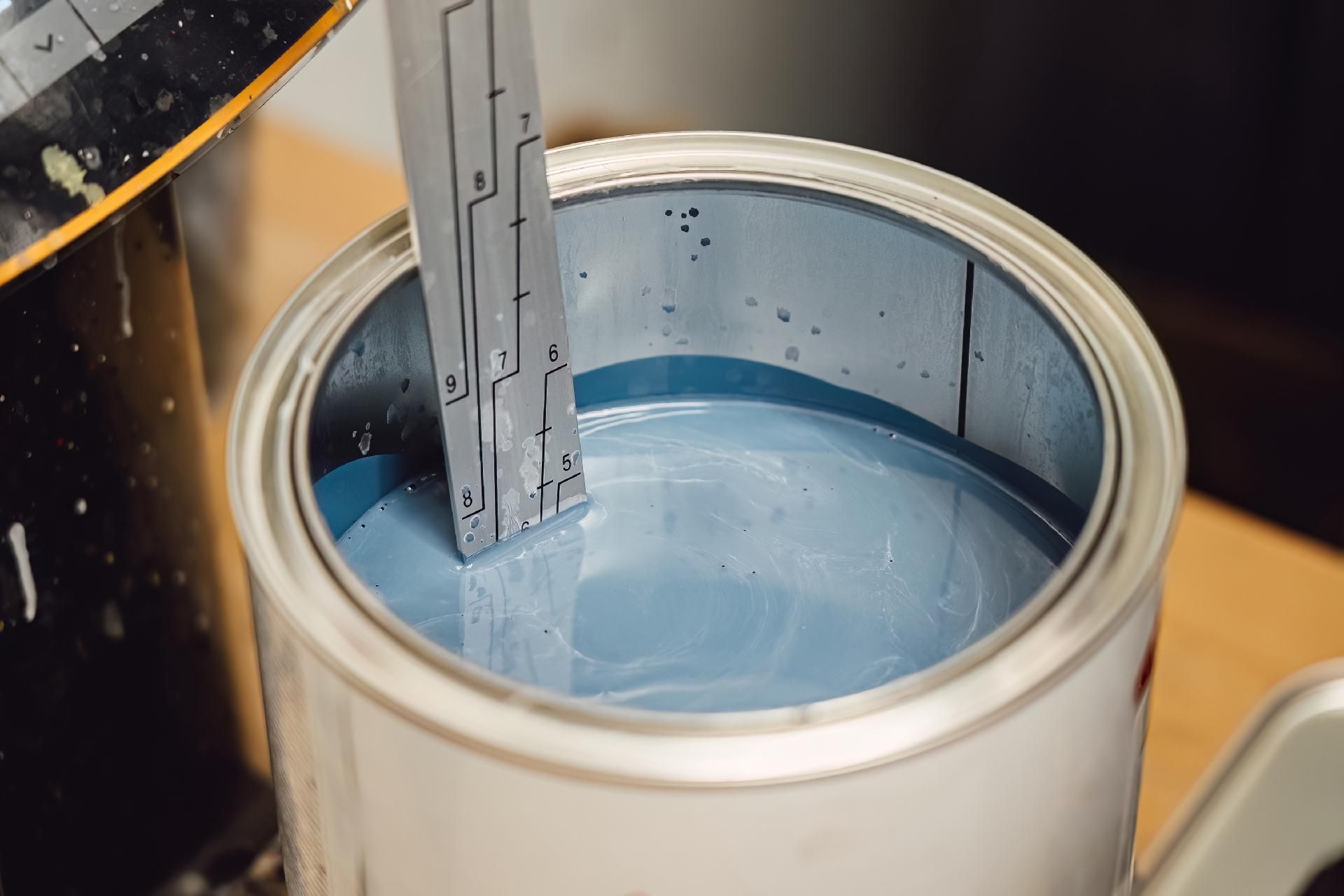 Eine Farbdose ist mit hellblauer Farbe gefüllt, während ein Metallwerkzeug hineingetaucht wird.