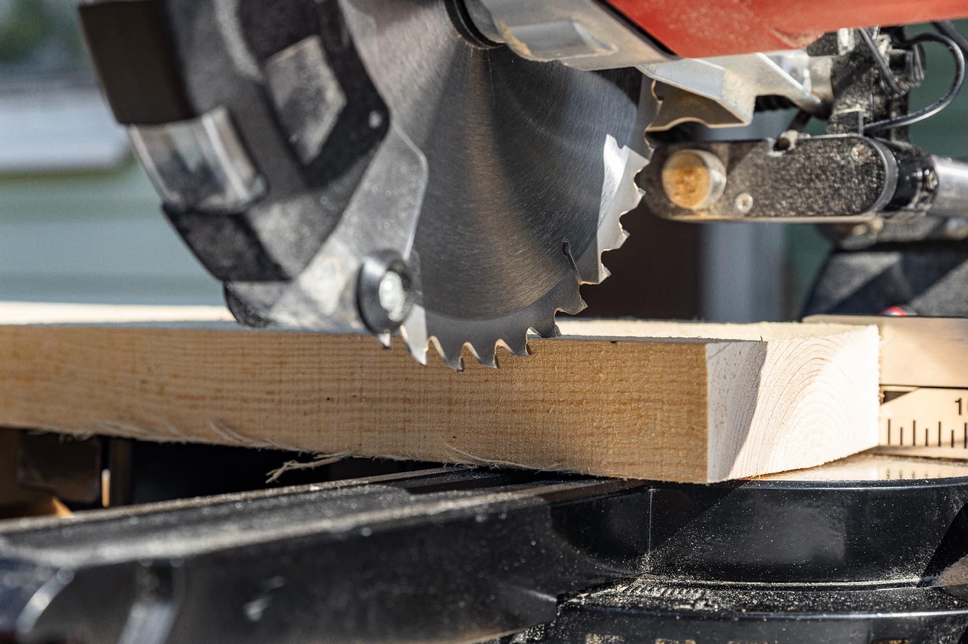 Nahaufnahme einer Kreissäge, die auf einer Werkbank ein Holzbrett durchtrennt.