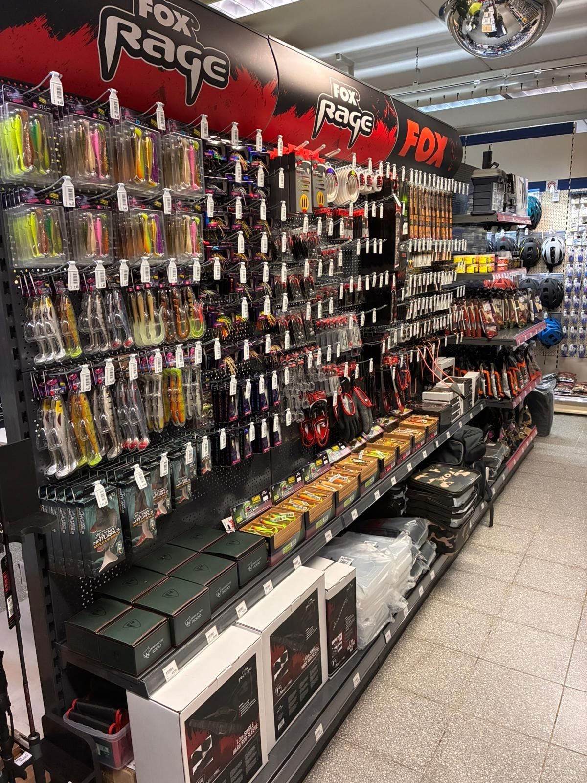 Ladenauslage mit farbenfrohen Angelködern Vollgepackte Ladenauslage mit farbenfrohen Angelködern und Zubehör, die an Lochwänden hängen, darunter Kisten.