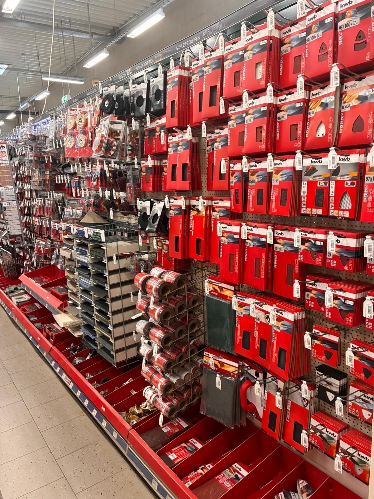 Ein Ladengang mit Reihen roter, verpackter Produkte in Verkaufsregalen unter hellem Deckenlicht.