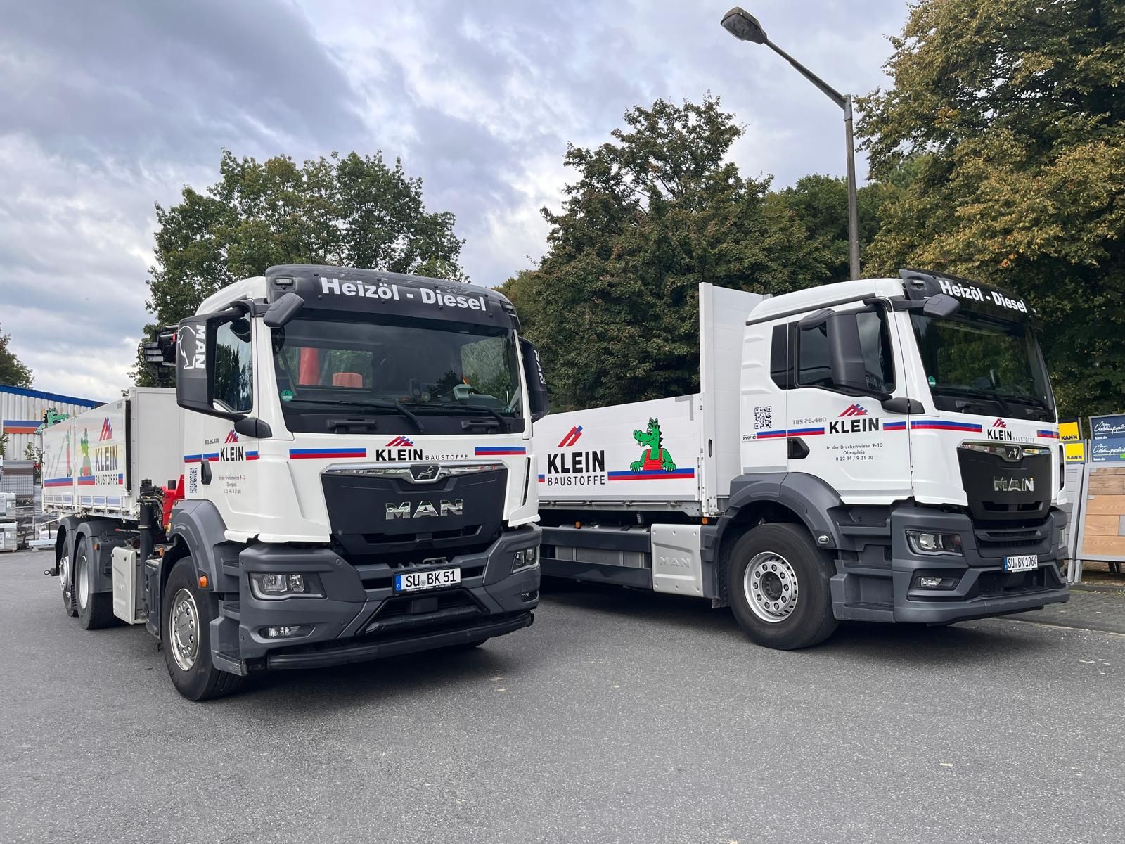 Zwei weiße Wagen stehen unter bewölktem Himmel nebeneinander auf einer Straße