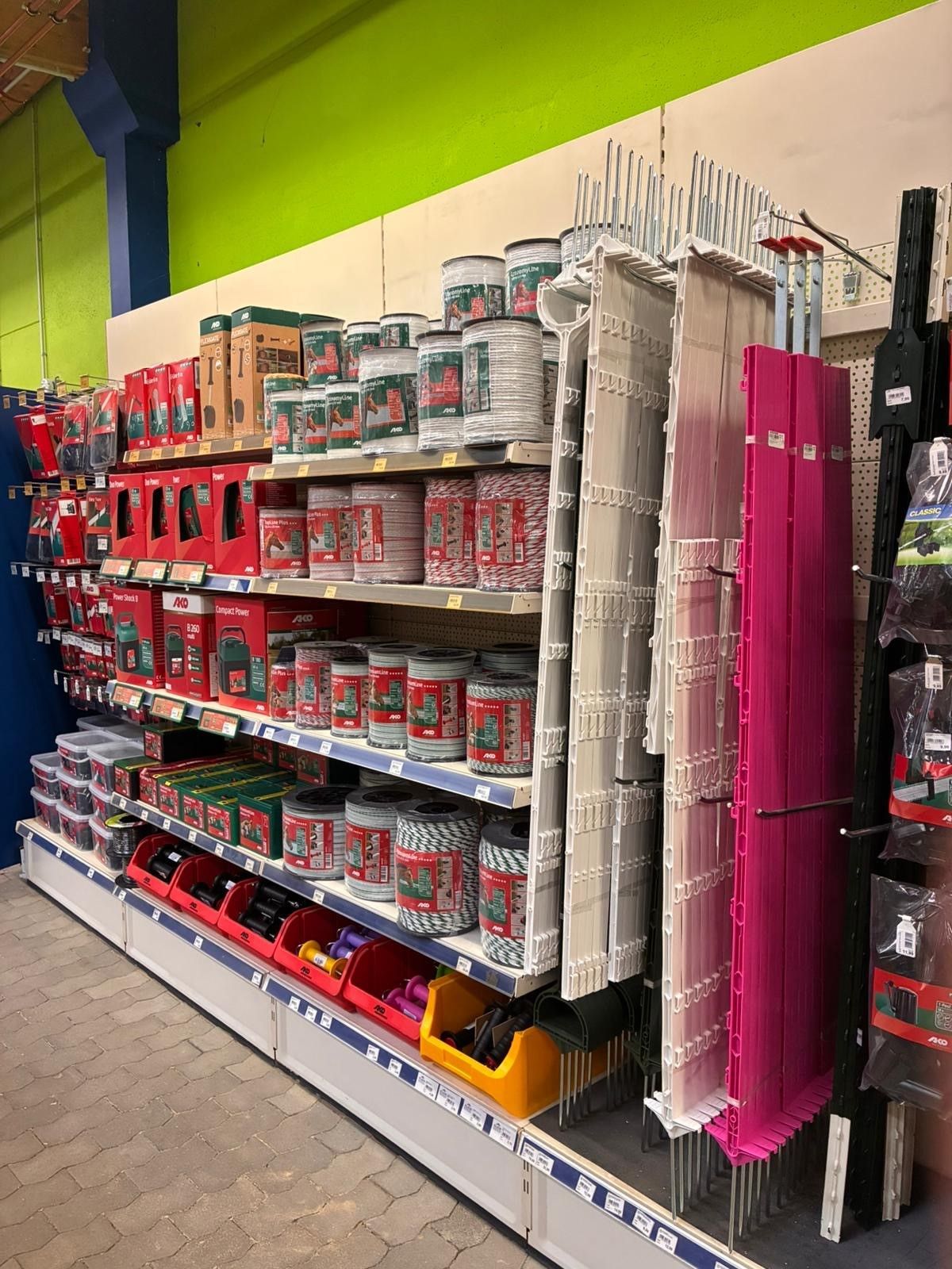 Ein Gang im Laden mit Regalen voller Farbdosen und Reinigungsmitteln sowie hängenden Wischmopps und Besen.