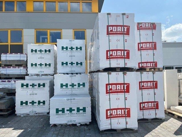 Vor einem Gebäude stehen gestapelte weiße Schiffscontainer mit der Aufschrift H+H und PORIT.