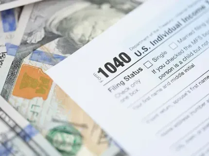 Un formulario 1040 de declaración de impuestos sobre la renta individual de EE. UU. está encima de una pila de dinero.