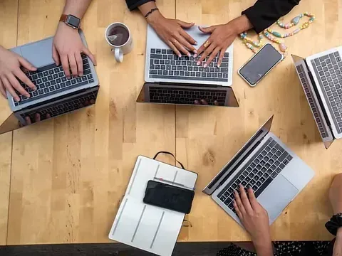 Un grupo de personas está sentada en una mesa usando computadoras portátiles.