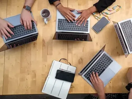 Un grupo de personas está sentada en una mesa usando computadoras portátiles.
