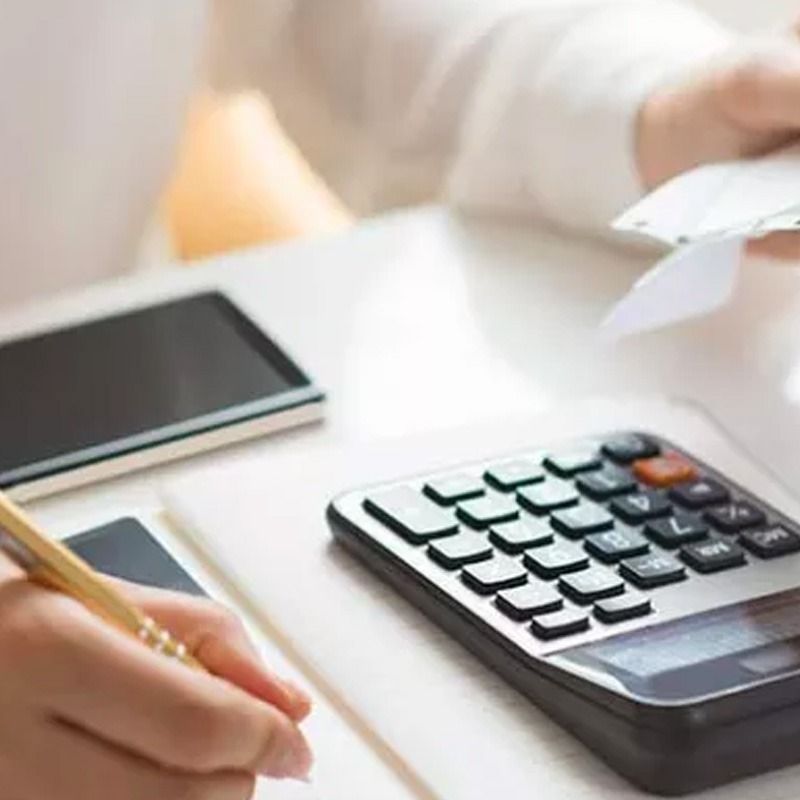 Una persona está escribiendo en un cuaderno al lado de una calculadora.
