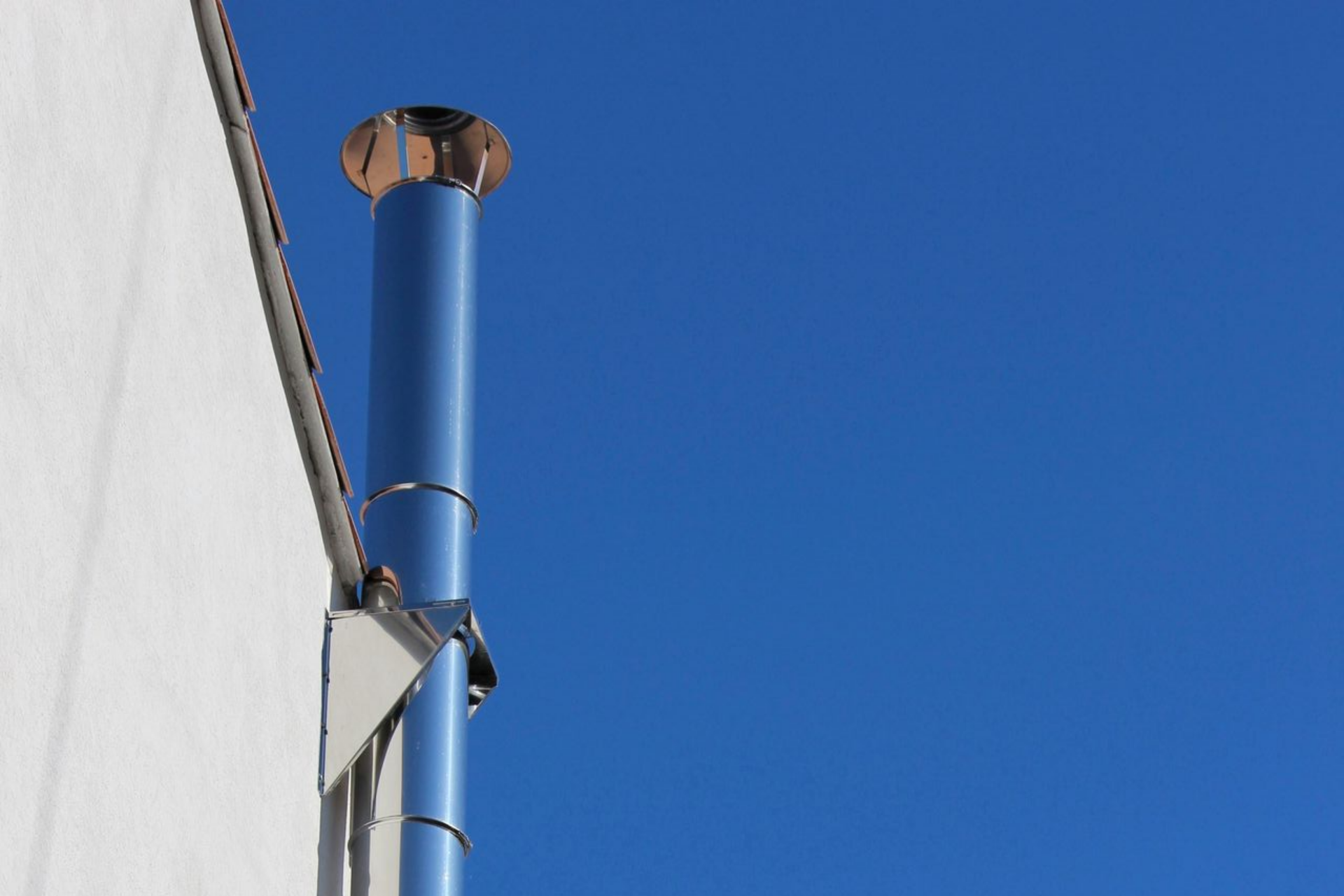 Conduit de cheminée chromé se détachant sur un ciel bleu vif, fixé sur un mur blanc.