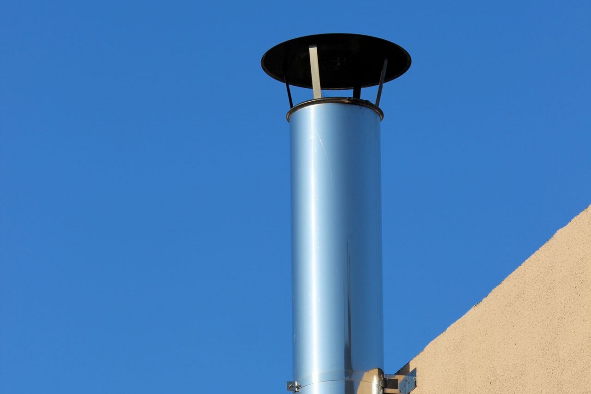 Cheminée métallique brillante se dressant vers le ciel bleu, montée sur un bâtiment beige.