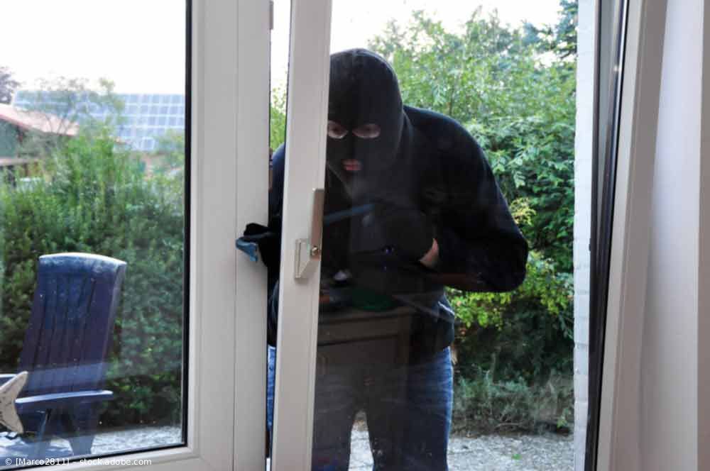 Maskierter Eindringling versucht, durch eine Glastür einzubrechen.