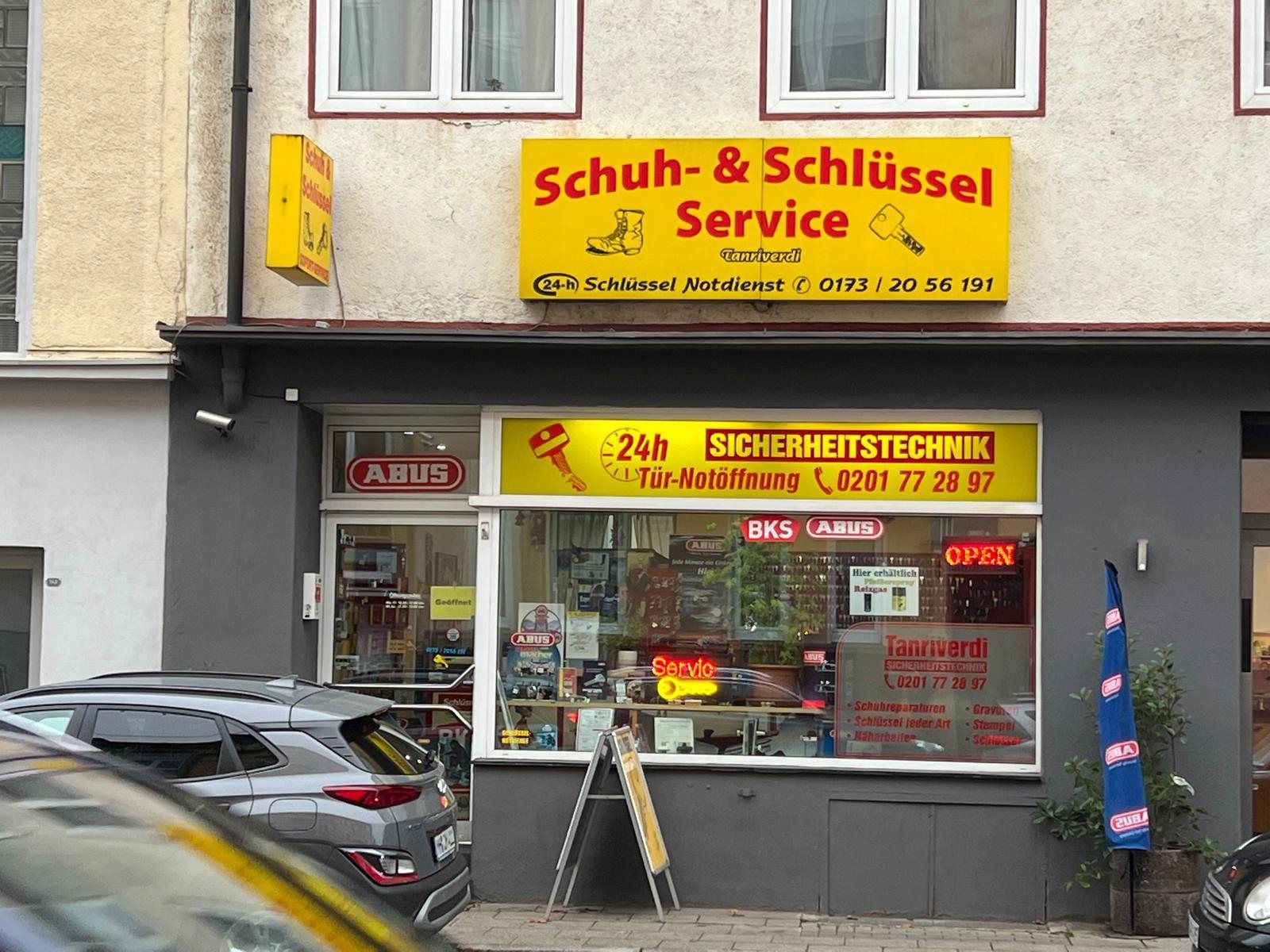 Schaufenster des „Schuh- & Schlüsselservice“ mit gelben Schildern und einem geparkten Auto auf der Straße