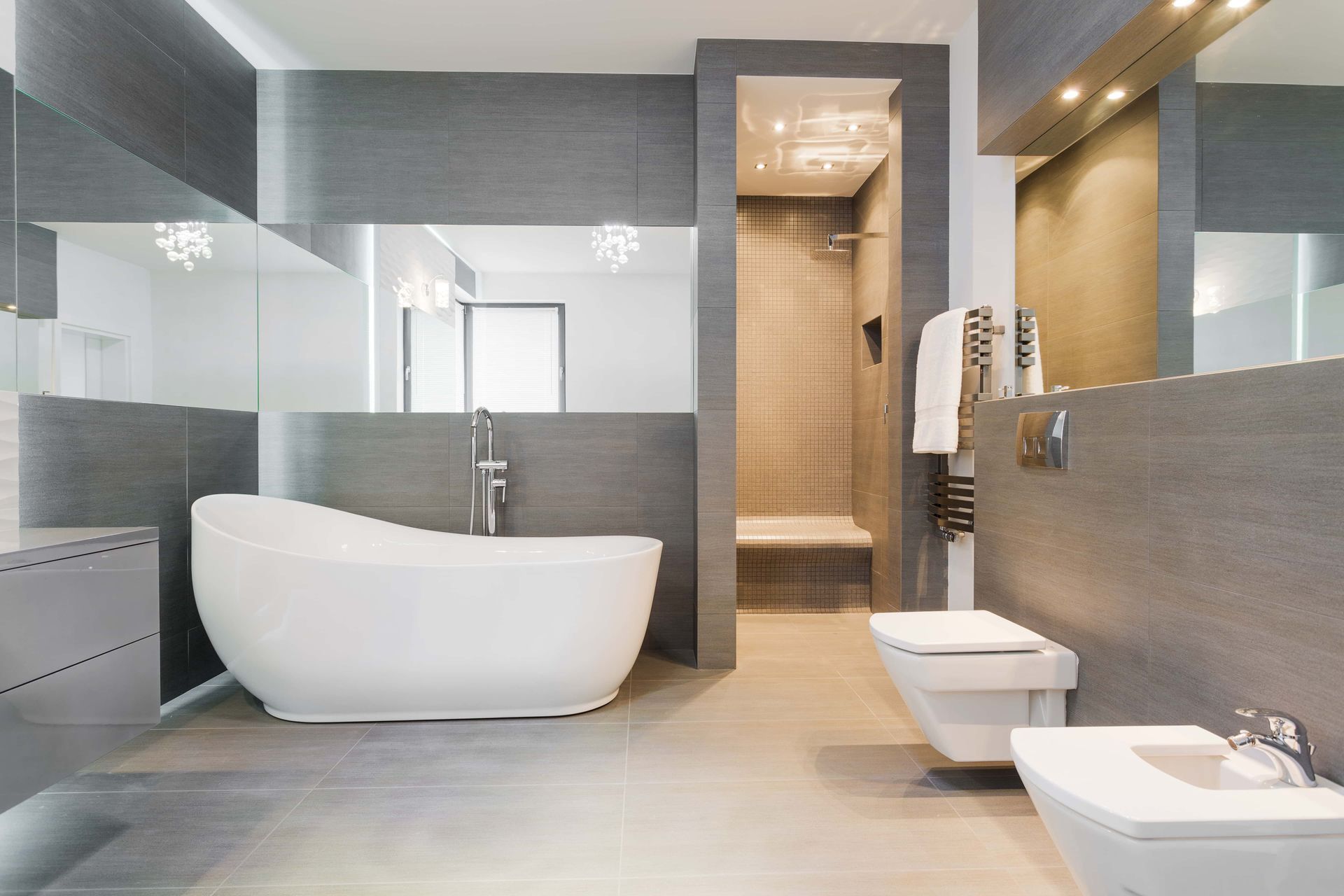 Salle de bains moderne grise avec baignoire îlot, douche et toilettes.
