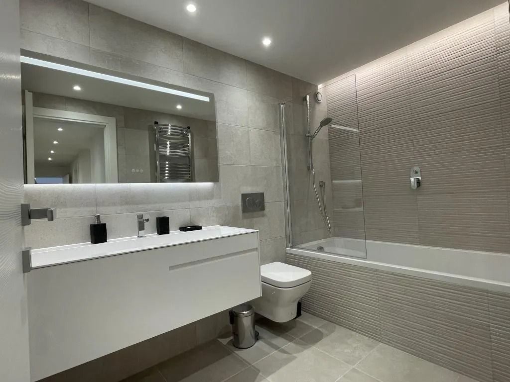 Salle de bains moderne avec carrelage gris, meuble-lavabo blanc, baignoire et toilettes.