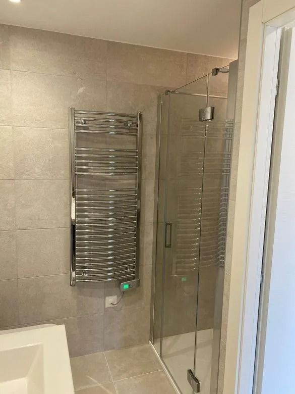 Salle de bains avec sèche-serviettes argenté, cabine de douche et carrelage aux tons neutres.